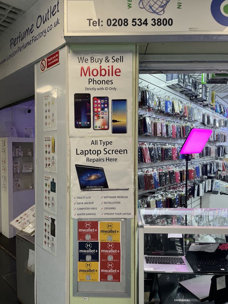 A We Buy and Sell Mobile Phones sign inside Connect, next to laptop screen repair advertising and a laptop being serviced on the counter